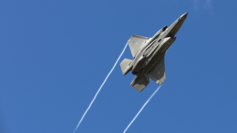 Royal Australian Air Force F-35A Lightning II aircraft flying at high speed against a clear blue sky. The aircraft is viewed from below and banking upward, with white vapour trails streaming from both wings. The image emphasises the aircraft's stealth design and airborne manoeuvrability, with no other aircraft or objects visible in the background.